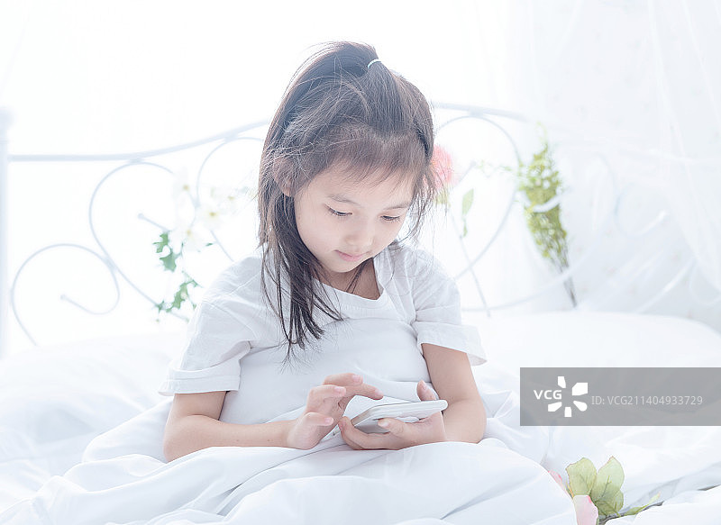 早晨起床坐在床上玩手机的小女孩图片素材