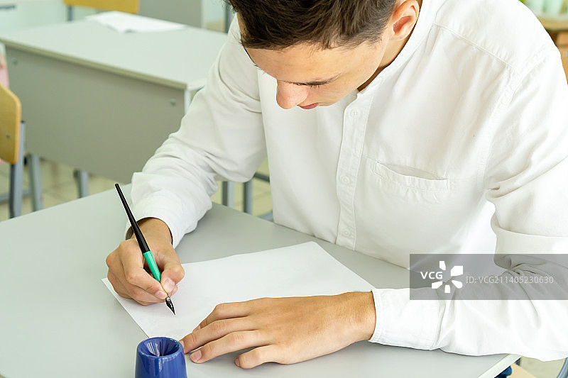 男学生在学校学习时用钢笔书写，坐着图片素材