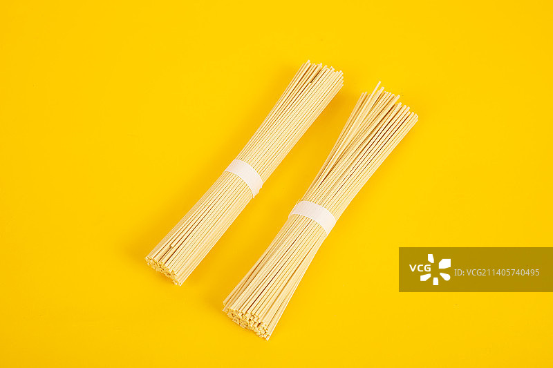 两捆细面条并排躺在黄色背景上图片素材