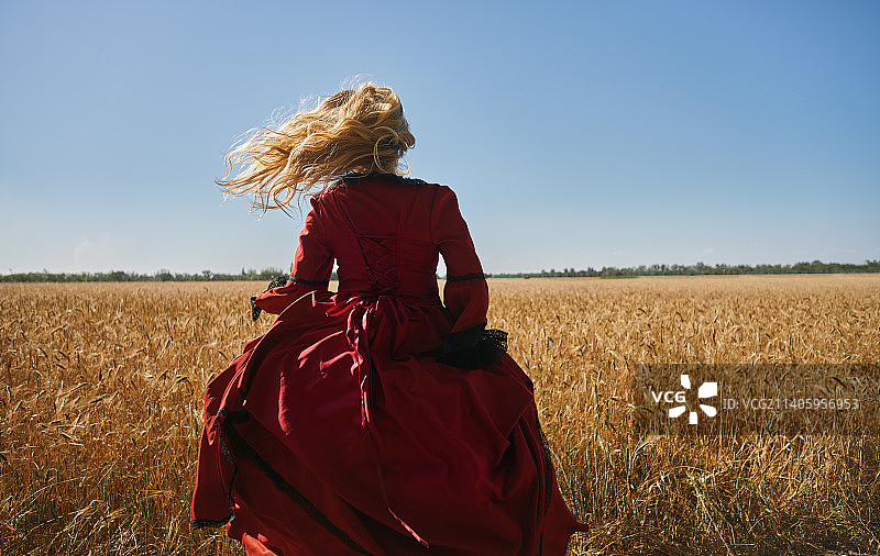 18世纪穿着红色维多利亚风格连衣裙在田野里奔跑的金发女人图片素材