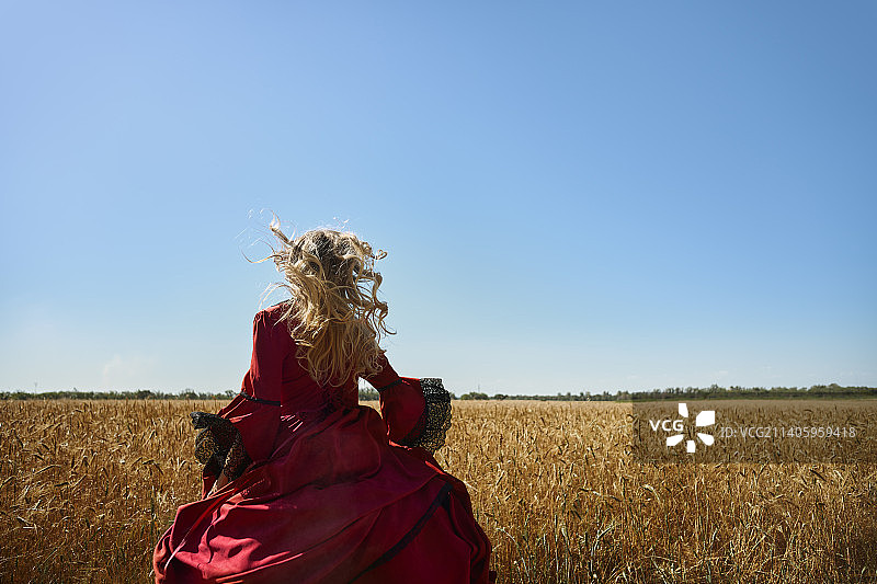 18世纪穿着红色维多利亚风格连衣裙在田野里奔跑的金发女人图片素材