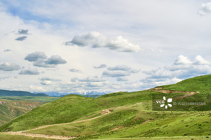 夏季多云天气下的山坡草地蜿蜒土路与远山图片素材