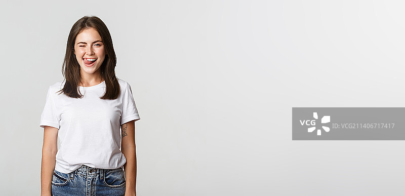 俏皮美丽的年轻女人眨眼吐舌，白色背景图片素材