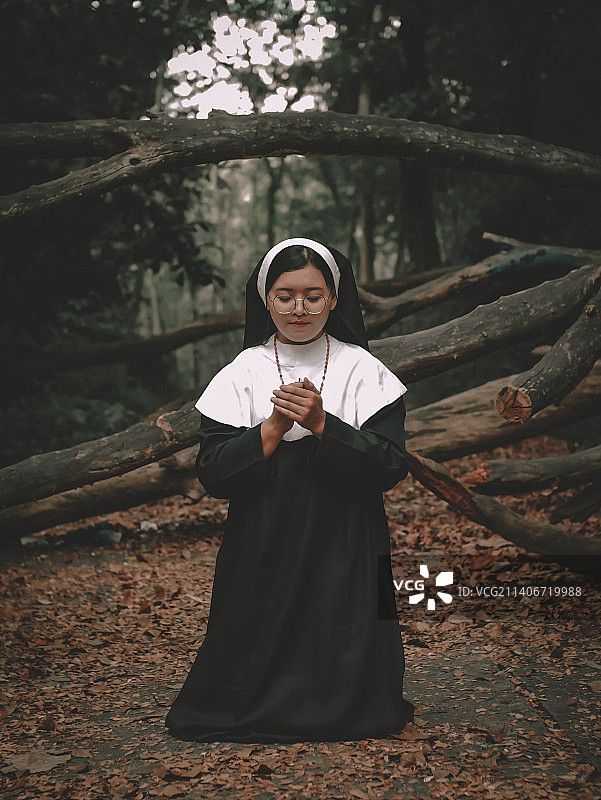 年轻女子身穿修女服装站在森林里的肖像图片素材
