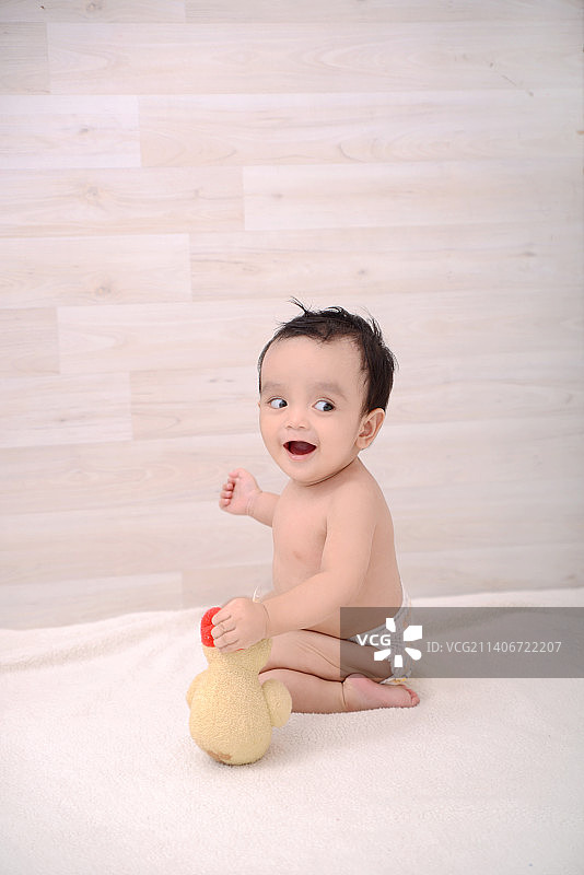 可爱的无上衣男婴坐在家中床上，印度尼西亚图片素材