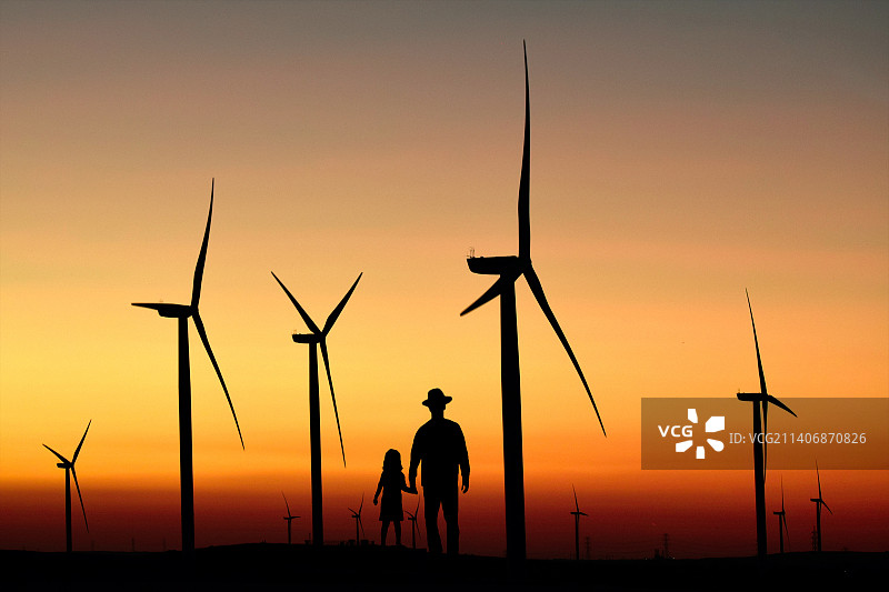 夕阳下风力涡轮机旁男人和孩子的轮廓图片素材