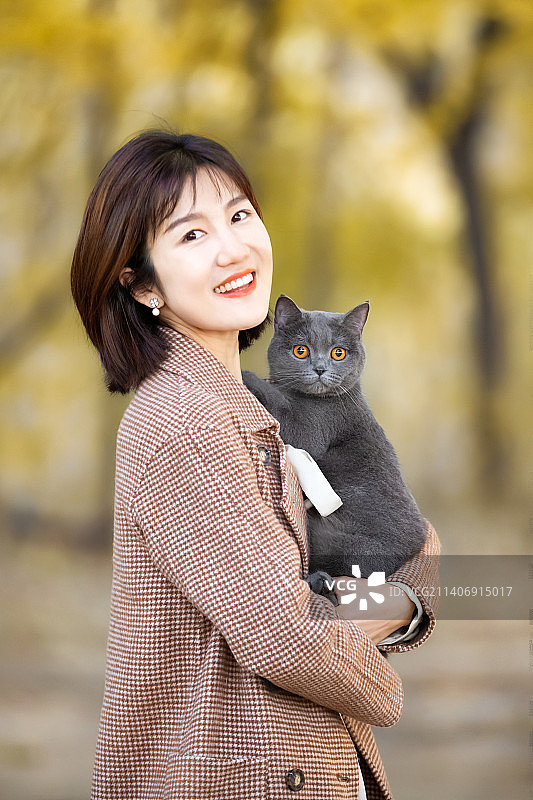 秋天公园里的抱着猫的年轻女人图片素材