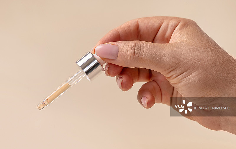 女人手持滴管在浅米色背景上滴液，医学研究图片素材