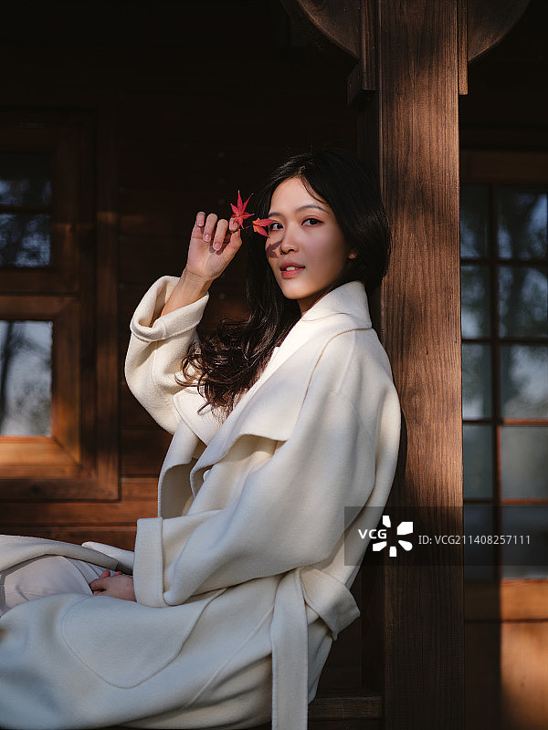 秋天小木屋前拿着枫叶的年轻女子图片素材