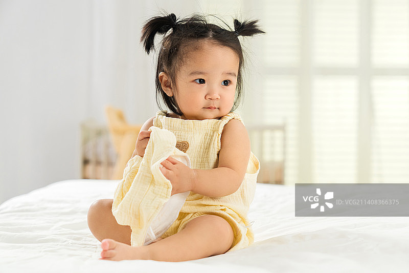 可爱的女宝宝坐在床上玩耍图片素材