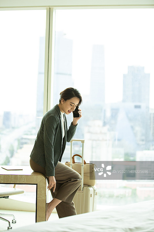 商务女人在酒店房间打电话工作，准备脱掉高跟鞋图片素材