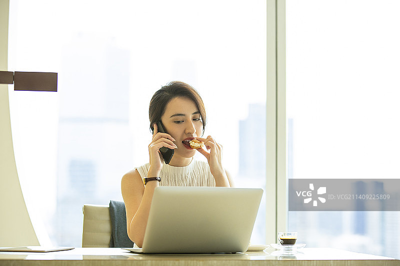 商务女子在酒店房间打电话和使用笔记本电脑、吃点心图片素材