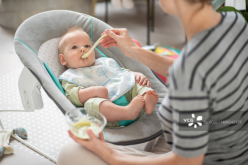 母亲用勺子喂坐在婴儿椅上的男婴图片素材