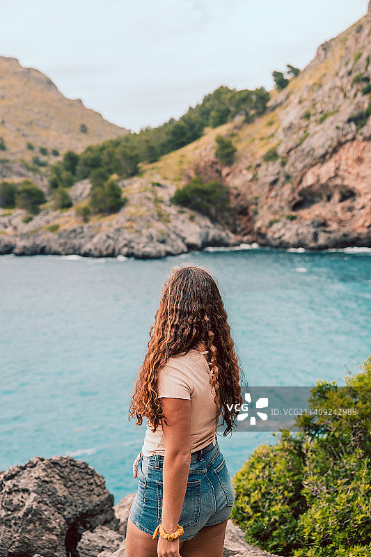 年轻卷发女子站在海边岩石上，西班牙巴利阿里群岛帕尔马的背影图片素材