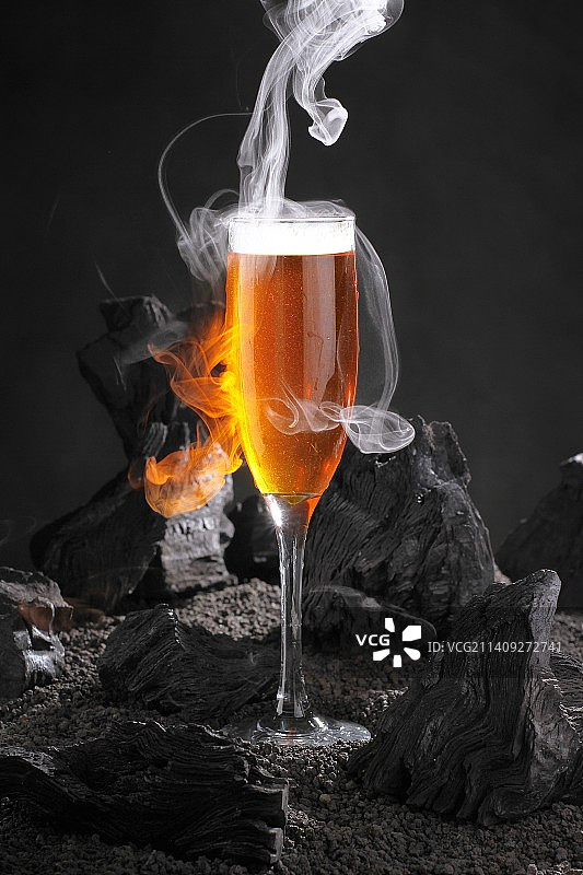 香槟笛玻璃杯中啤酒的特写，黑色木炭桌子上有烟雾图片素材