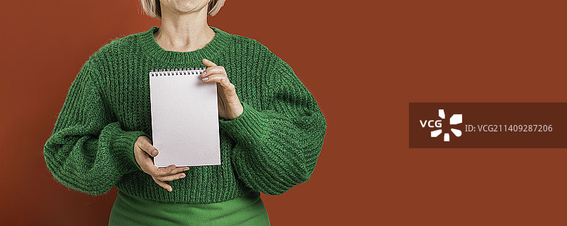 在红色背景下，身穿绿色毛衣的女人拿着记事本图片素材