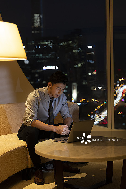 夜晚商务男子在酒店房间使用笔记本电脑加班图片素材