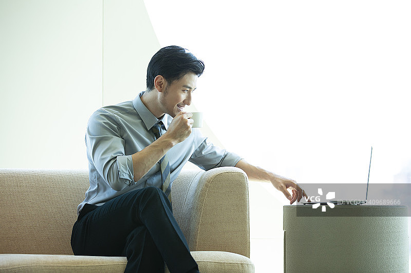 商务男子在酒店房间喝咖啡、使用笔记本电脑工作图片素材