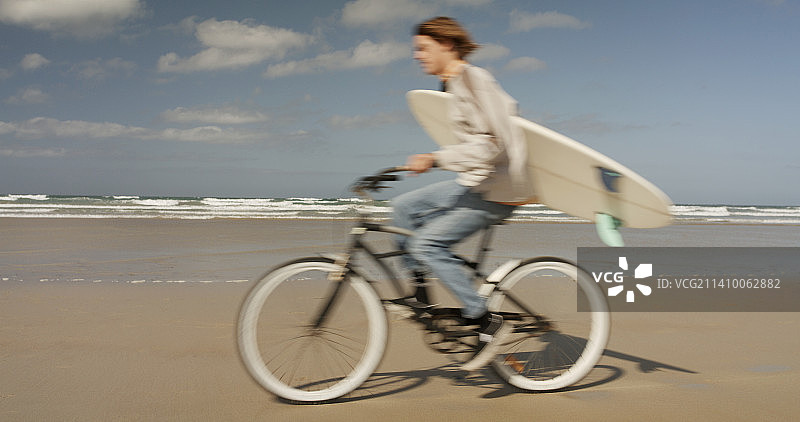 冲浪者骑自行车沿着海滩前往他最喜欢的断浪处图片素材