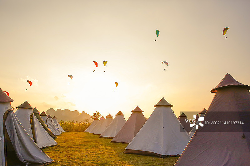 温暖光线下的南宁大明山露营基地和空中飞翔的滑翔伞图片素材