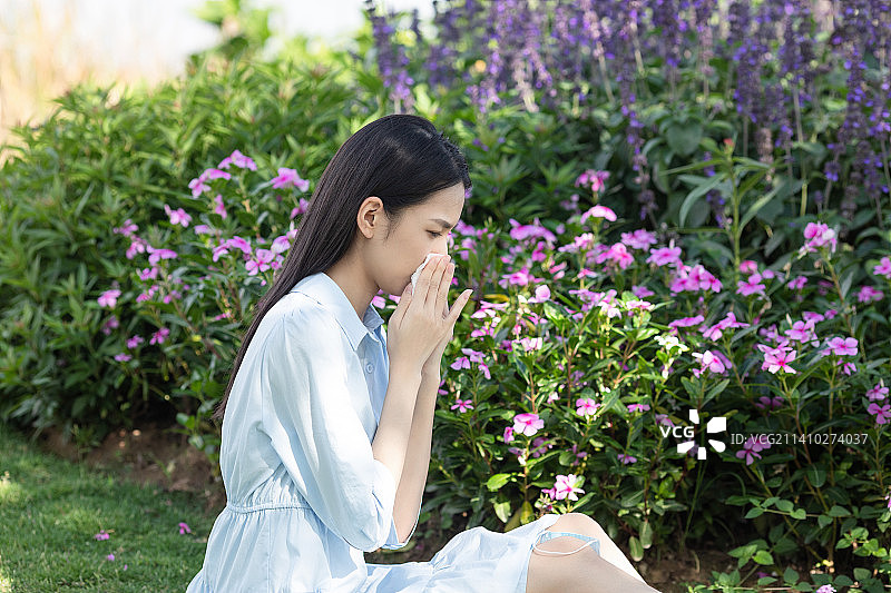一名年轻女性在花丛旁用纸巾擦鼻子图片素材