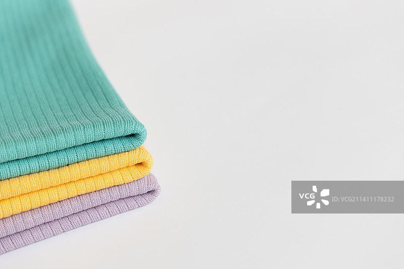 白色背景上堆叠的紫色、黄色、绿色婴儿棉质服装图片素材