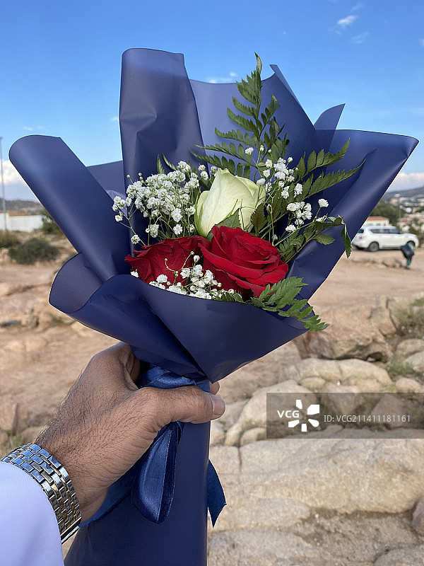 男人手持鲜花，背景是蓝天图片素材