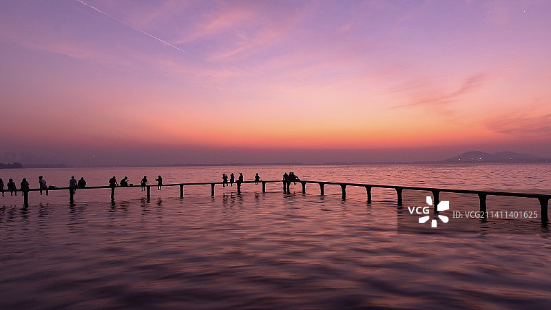 日落时海滩上的人们在天空的映衬下剪影图片素材