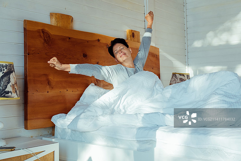 微笑的可爱女孩坐在舒适的床上伸展身体图片素材