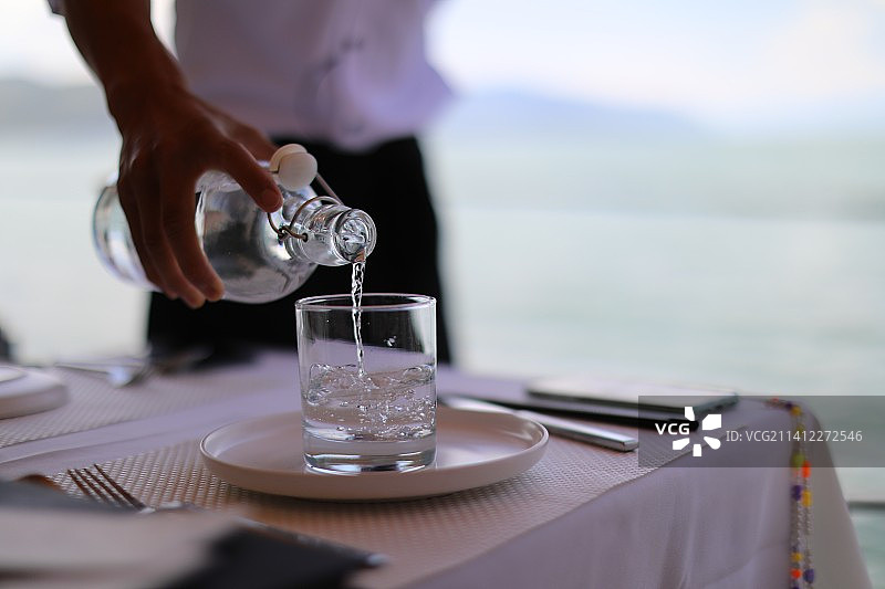在桌子上往玻璃杯里倒水的人的中间部分图片素材