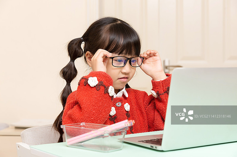 室内书桌前用笔记本电脑上网课的亚洲小学生图片素材