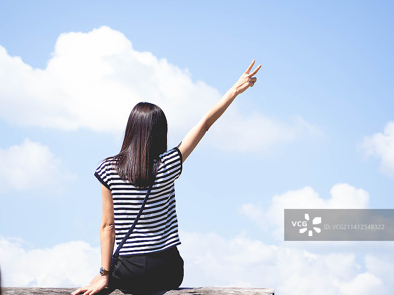 在泰国，一位女士抬起手臂，对着明亮的天空比出两根手指。图片素材