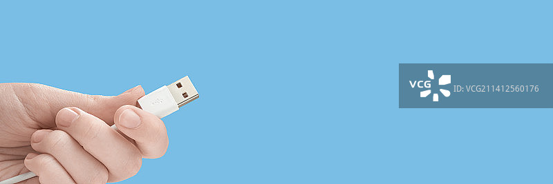 手指 holding 蓝色背景上的白色Type-C连接线图片素材