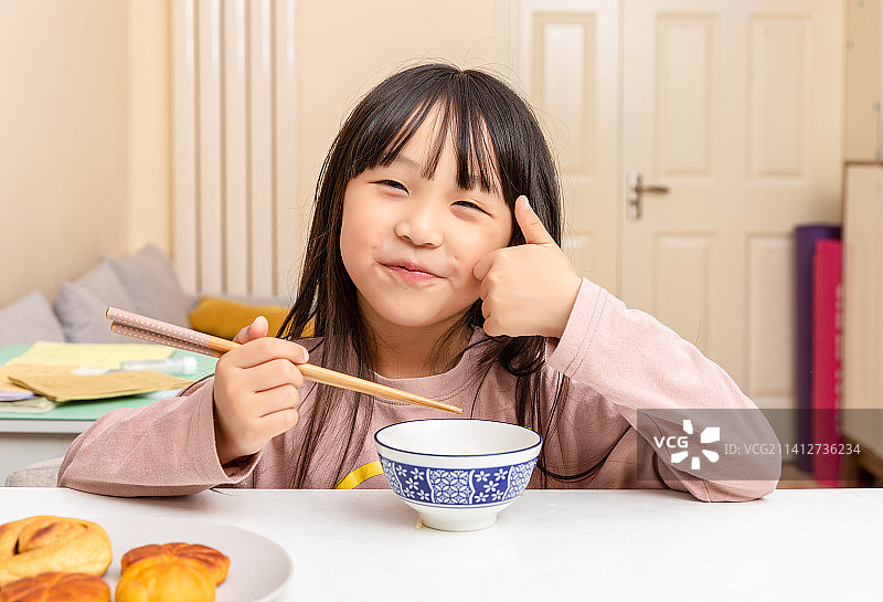 室内白色餐桌前吃饭的小女孩伸出大拇指图片素材