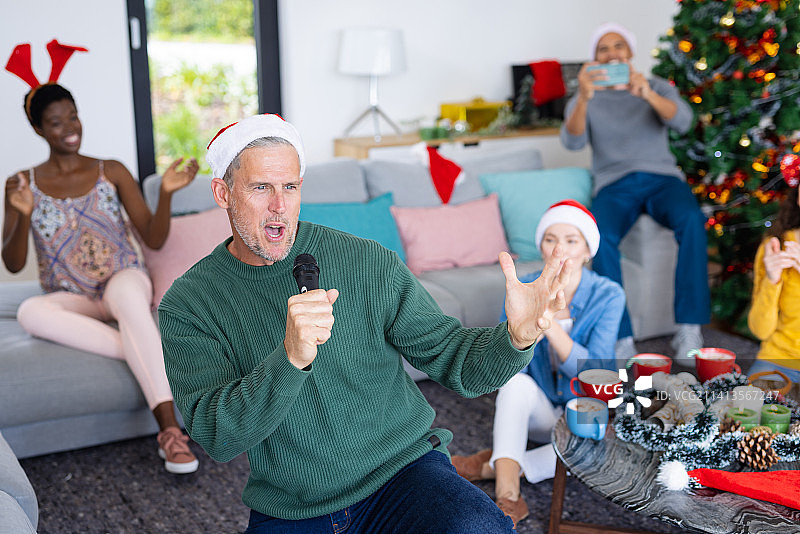 快乐的白人男子在家中与不同的朋友一起唱歌庆祝圣诞节卡拉OK图片素材