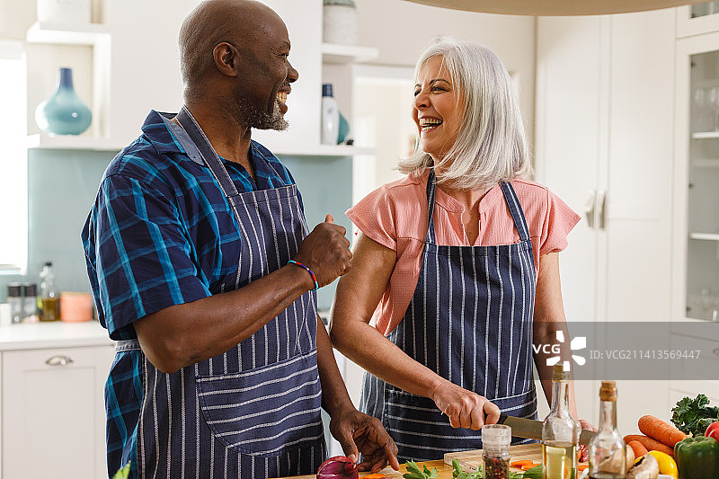 快乐的老年夫妇在厨房里穿着围裙做饭图片素材