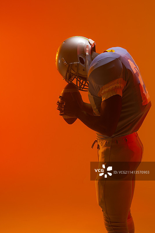 拿着球的非裔美国男子橄榄球运动员，带有霓虹橙色灯光图片素材