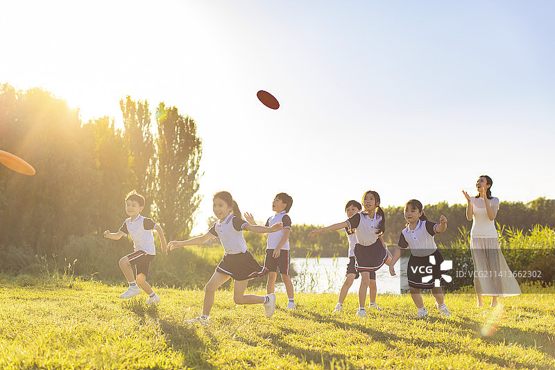 快乐的小学生和老师在草地上玩飞盘图片素材