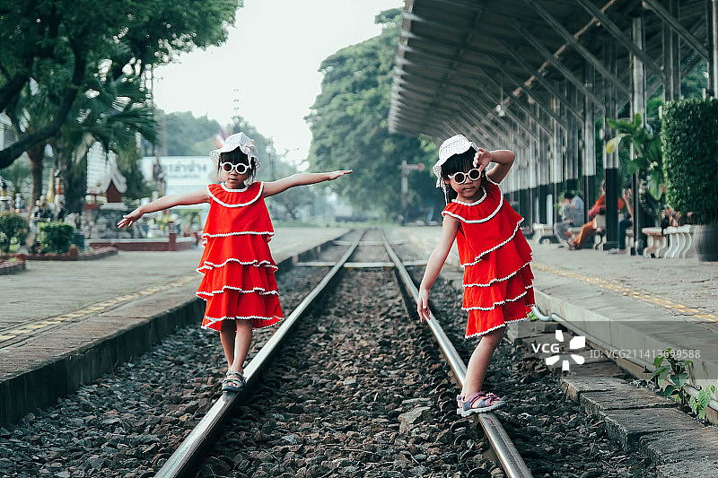 在泰国，两个穿着红色连衣裙的小姐妹走在夏日的铁轨上图片素材