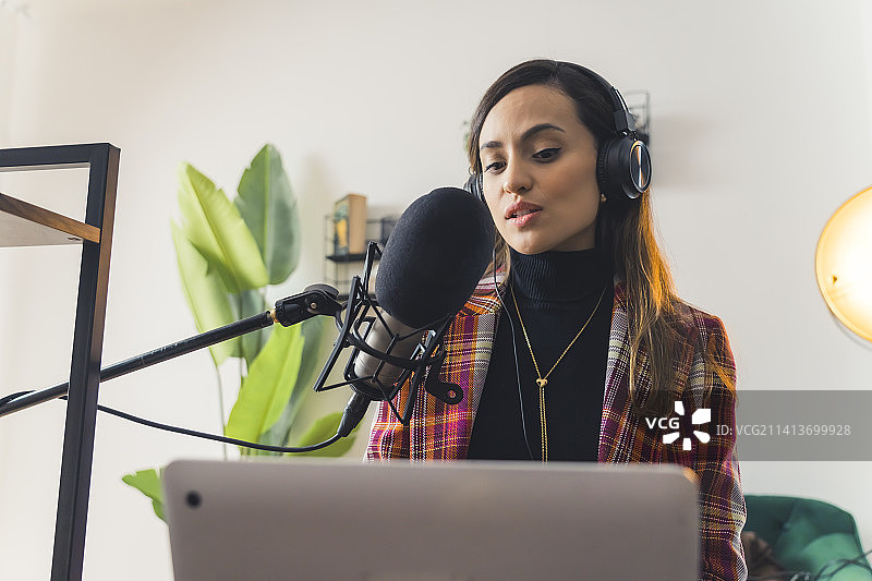 在家里的工作室里录制播客的年轻快乐的棕发女子图片素材