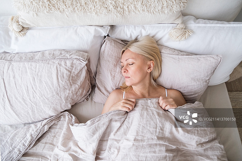 一位中年妇女躺在家里床上睡觉的俯视图图片素材