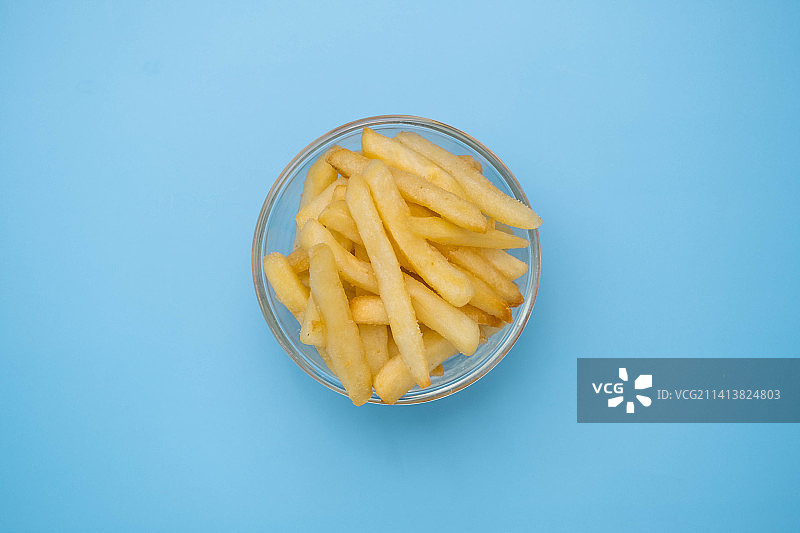 浅蓝色背景下玻璃碗中炸薯条的俯视图图片素材