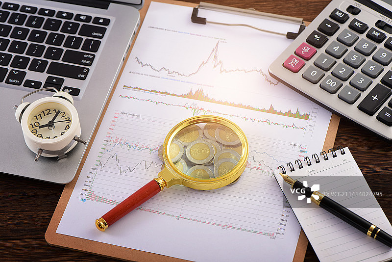股市图表上放着笔记本电脑、放大镜、时钟、硬币、钢笔和计算器图片素材
