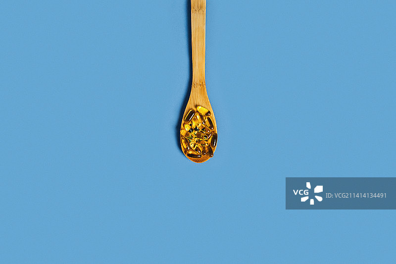 蓝色背景上的装有胶囊的木勺图片素材