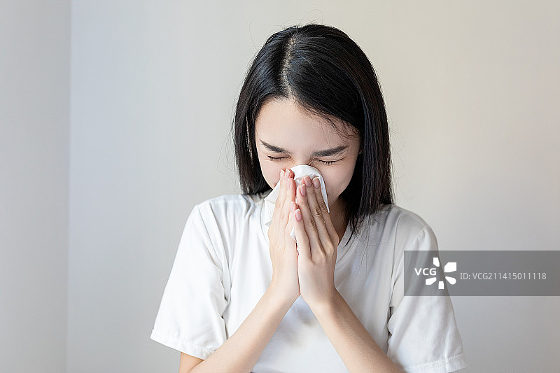 室内一名年轻的亚洲美女感冒用纸巾擦鼻子图片素材