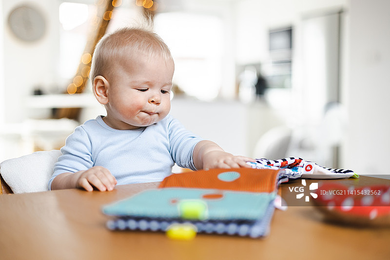 快乐的婴儿坐在餐桌旁玩玩具图片素材