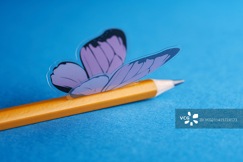 人造蝴蝶停留在蓝色背景的黄色铅笔上（马来西亚）图片素材