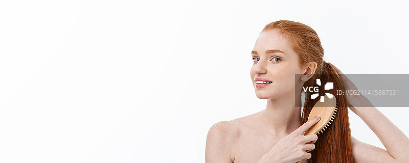 快乐微笑的姜黄色雀斑年轻女性梳理长发的照片图片素材