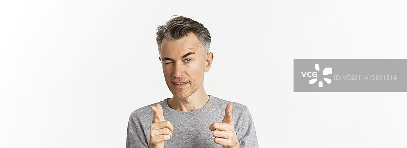 近距离拍摄的英俊灰发男子，眨眼并指向前方图片素材