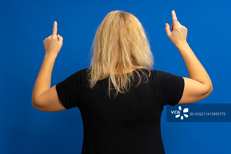 穿着黑色T恤的金发白人女子从背后转过身来并指向图片素材